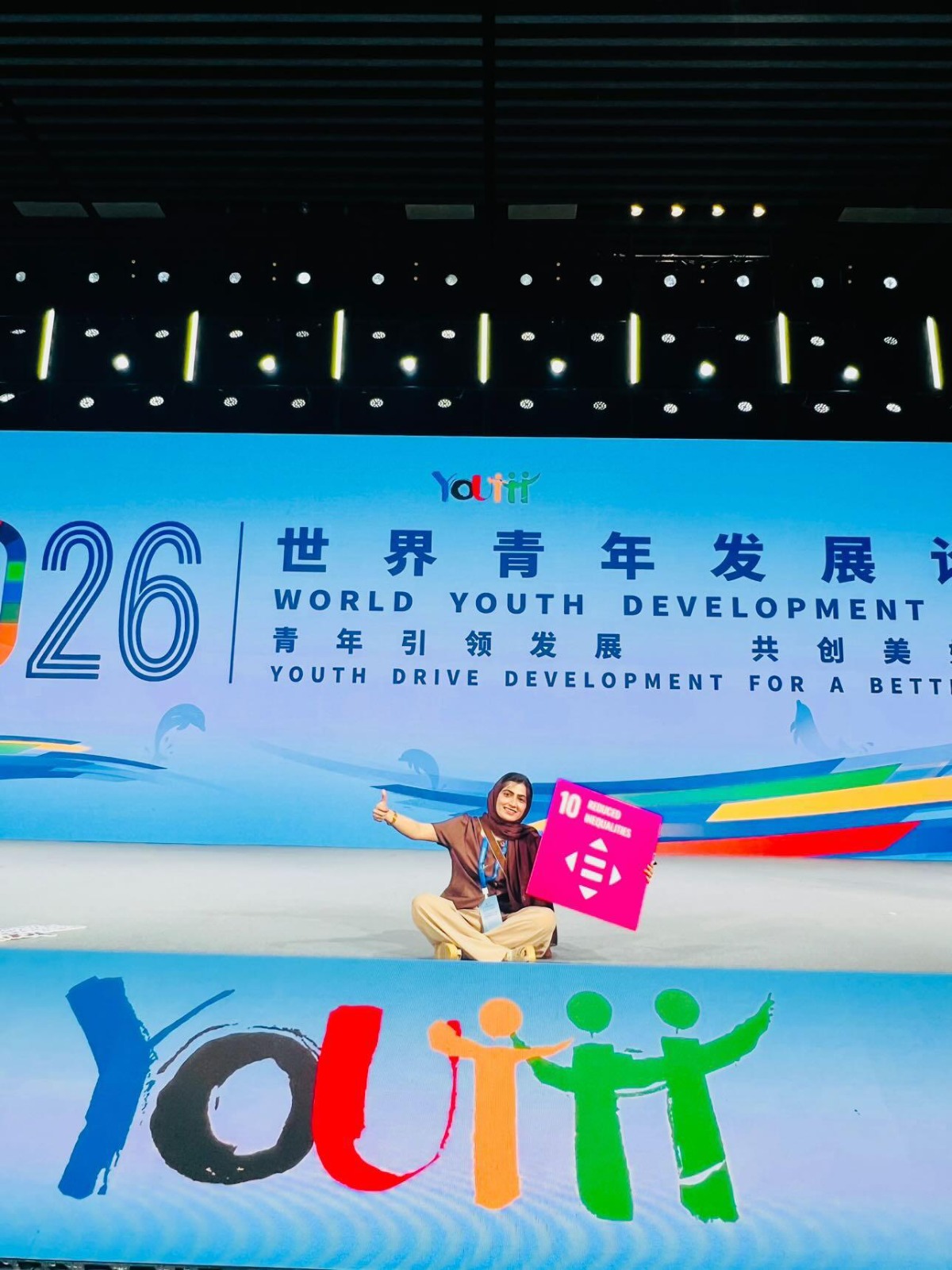 Farah Gul Rahuja on stage at the World Youth Development Forum holding an SDG 10 placard